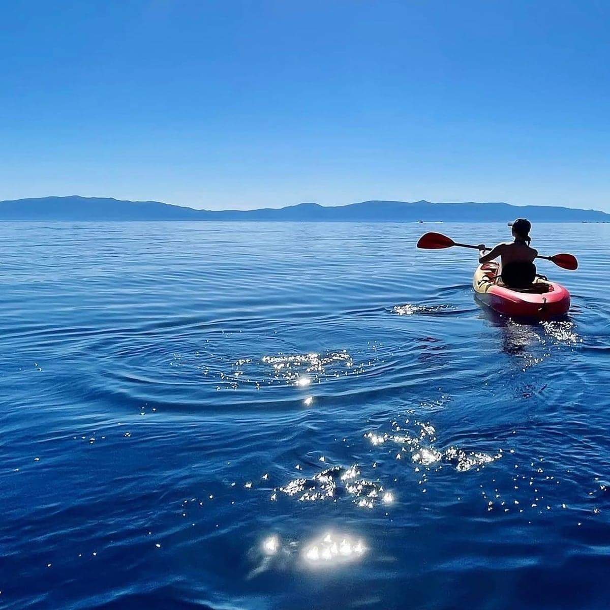 Dr. Ross-Nash paddling a red kayak across calm blue water toward distant mountains