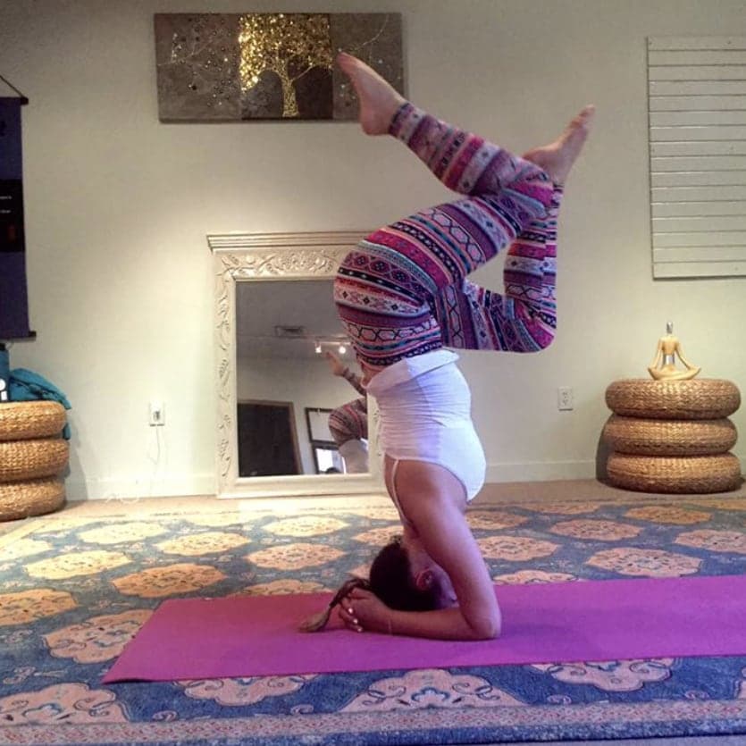 Dr. Ross-Nash in a forearm headstand on a yoga mat, legs folded overhead